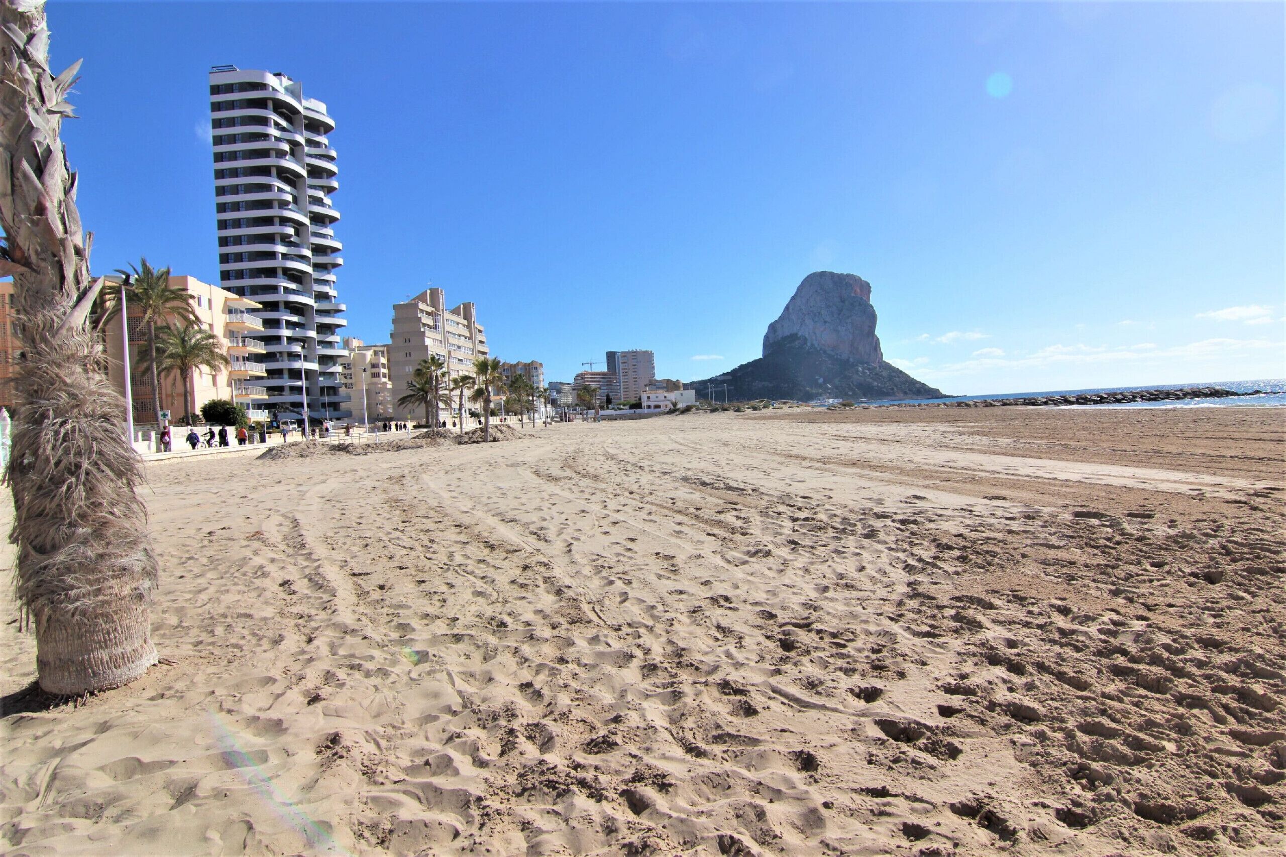 Ein Strand mit einem hohen Gebäude, Palmen und einer felsigen Klippe.