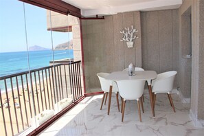 Ein Balkon mit weißem Tisch und Stühlen, einer Kakteendeko und Blick auf Strand und Meer.