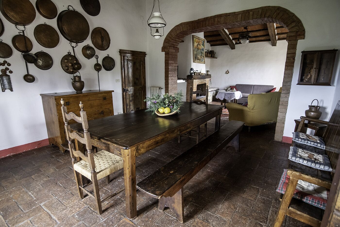 Ein rustikaler Essbereich mit Holztisch und Bänken, umgeben von Steinmauern und einem Kamin aus Ziegelsteinen.