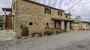A stone building with a tiled roof, a wooden door, and a gravel driveway. -  Manor house + studio apartment (Montiano)