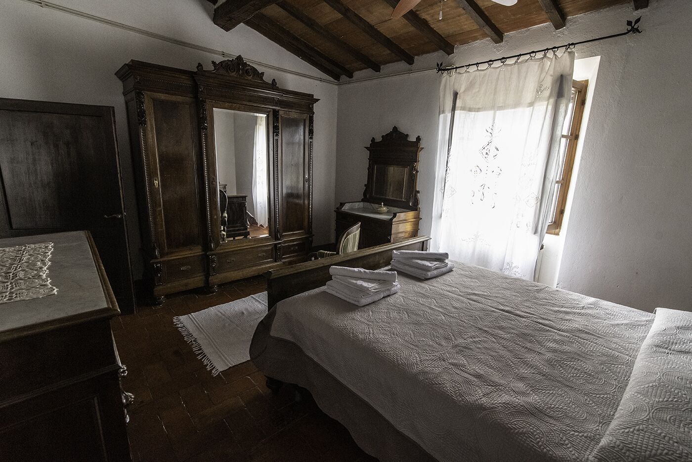 Ein Schlafzimmer mit einem großen Bett, einem Holzschrank, einem Spiegel und einem Fenster mit Vorhängen.