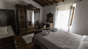 A bedroom with a large bed, a wooden wardrobe, a mirror, and a window with curtains. -  Manor house + studio apartment (Montiano)
