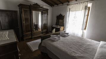 Ein Schlafzimmer mit einem großen Bett, einem Holzschrank, einem Spiegel und einem Fenster mit Vorhängen.