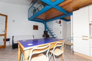 A dining area with a blue-tiled table, wooden chairs, a staircase with blue railings, and white cabinets.
