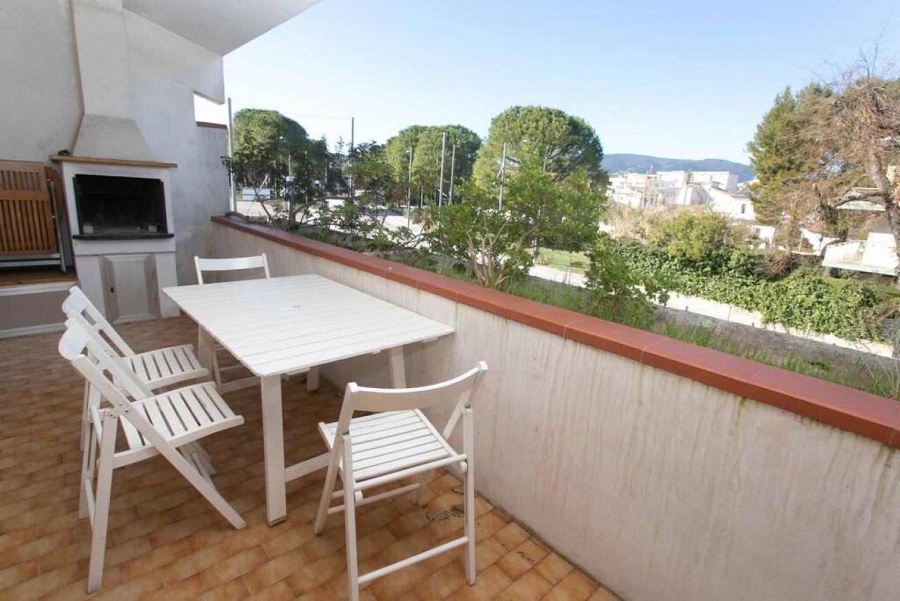 A balcony with a table and chairs, a grill, and a view of a residential area.