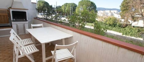 A balcony with a table and chairs, a grill, and a view of a residential area.