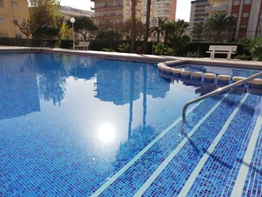 A clear swimming pool with blue mosaic tiles, a metal pool ladder, and benches around the perimeter.