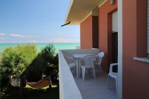 Un balcón con muebles de plástico blanco, una hamaca y vista al mar.