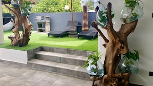 Un espace extérieur moderne avec une pelouse artificielle, des chaises longues et un parasol rouge.