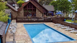 Piscina rectangular con solárium de piedra, rodeada por una valla de madera y sillas de descanso.