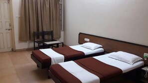 Una habitación de hotel con dos camas individuales, una silla, una mesita y una ventana con cortinas.