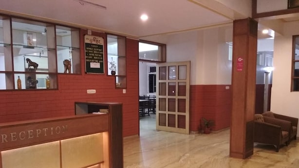 A reception area with a marble floor, a reception desk labeled "RECEPTION," and a glass display case with items. - Hotel Durvankur (Ratnagiri)