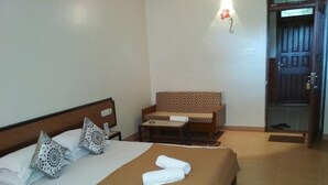 A neatly made bed with a brown bedspread and two pillows, a small table with a chair, and a wall-mounted light fixture. - Hotel Durvankur (Ratnagiri)