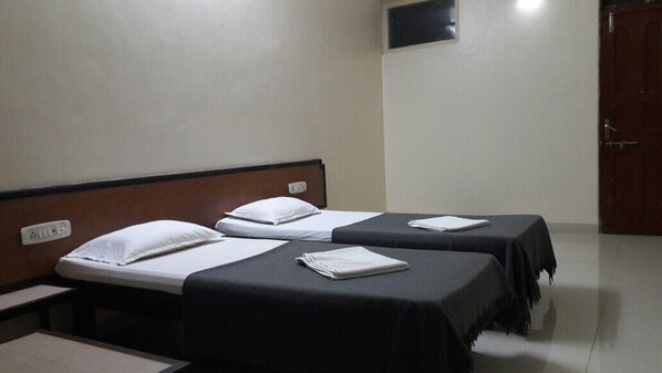 Habitación de hotel con dos camas individuales, cada una con una almohada y un edredón doblado.