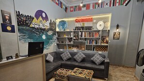A living room with a sofa, ottomans, a bookshelf, and a wall with international flags. - Cheers Hostel Cairo (Cairo)