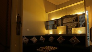 A dimly lit room with a patterned bench, a wall-mounted shelf with decorative items, and a patterned rug. - Cheers Hostel Cairo (Cairo)