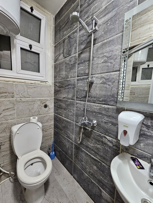 A bathroom with a toilet, a sink, a shower with a handheld showerhead, and a soap dispenser. - Cheers Hostel Cairo (Cairo)