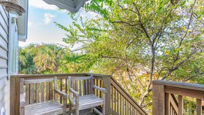 A wooden deck with a bench and a railing, surrounded by trees and a house.