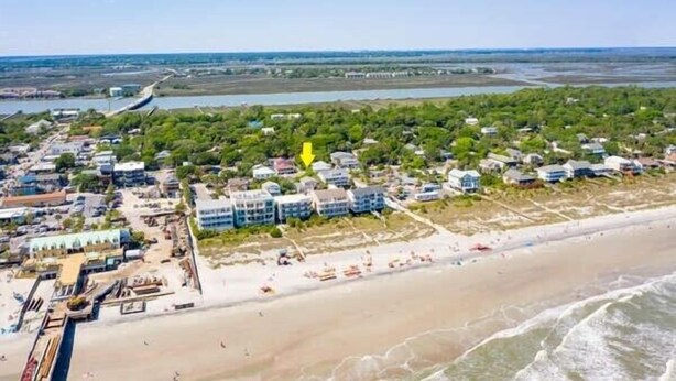 An aerial view of a coastal area with a beach, residential buildings, and a marina.