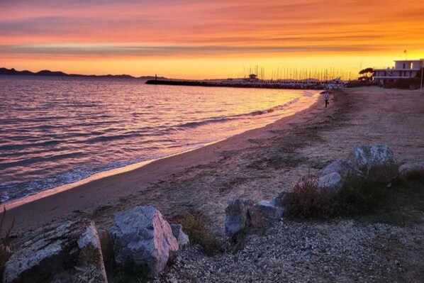 En strand med en stenet kystlinje, roligt vand og en solnedgangshimmel.