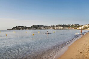 A beach with calm waters, a sandy shore, and a distant town.