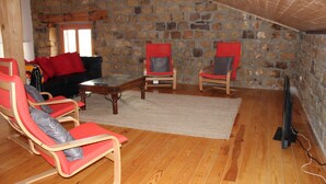 A cozy living room with a stone wall, wooden flooring, and red and grey upholstered chairs.