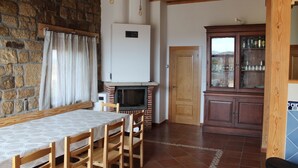 A dining area with a table and chairs, a fireplace, a kitchen with cabinets, and a stone wall.