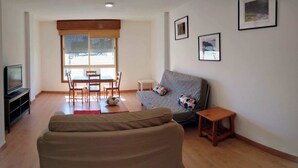 A living room with a sofa, a television, a dining table with chairs, and a small wooden stool. - Centric Three Bedroom Flat in Santa Cruz 5B (Santa Cruz de Tenerife)