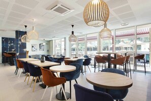 A modern dining area with round tables and chairs, pendant lighting, and large windows offering views.