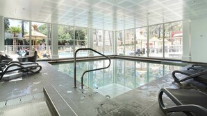 An indoor swimming pool with clear glass walls, a tiled floor, and a ceiling with a geometric pattern. - Cozy & Contemporary Stay (Cavalaire sur Mer)