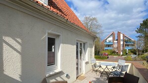 A patio area with wicker furniture and a table, a building with a red-tiled roof, and a clear blue sky. - Immediately on the beach! (Kiel)