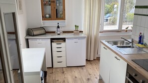 A modern kitchen with white cabinets, a built-in oven, a sink, and a window with a view of the outside. - Immediately on the beach! (Kiel)