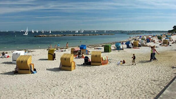 A beach with yellow beach huts, a sandy shore, and sailboats in the water. - Immediately on the beach! (Kiel)
