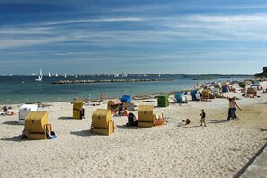 A beach with yellow beach huts, a sandy shore, and sailboats in the water. - Immediately on the beach! (Kiel)