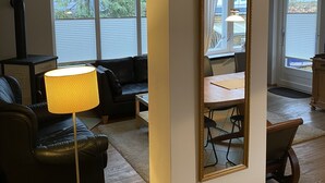 A living room with a black leather sofa, a small wooden table, a floor lamp, and a large mirror on the wall. - Immediately on the beach! (Kiel)