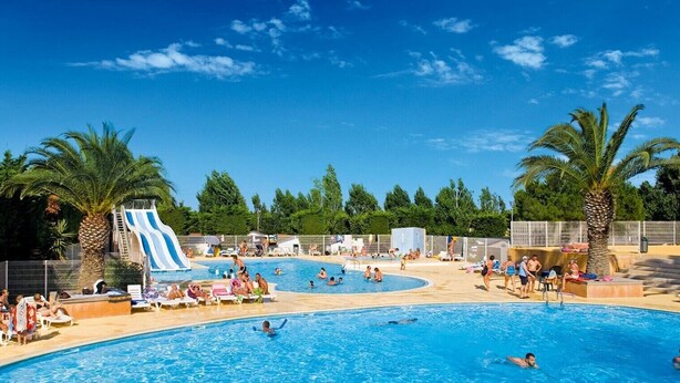 Un área de piscina con sillones de descanso, un tobogán y palmeras.