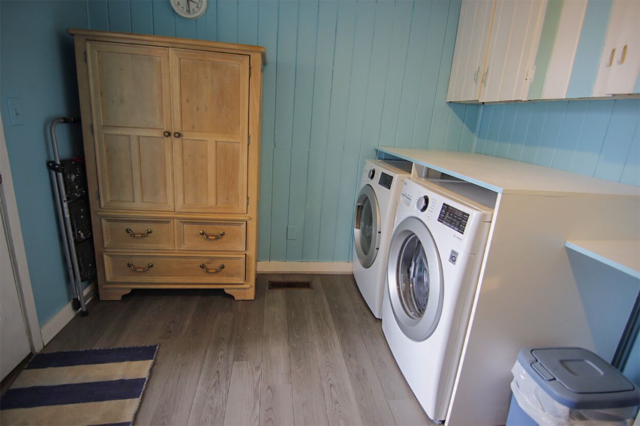 Une buanderie équipée d’un meuble en bois, d’un lave-linge et d’une poubelle.