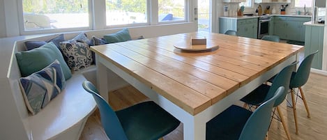 A dining area with a wooden table and blue chairs, a built-in bench with cushions, and a kitchen in the background.