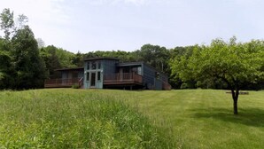 A two-story house with a balcony, surrounded by a grassy field and trees. - Mid-Century Home Surrounded by Meadows (Pine Plains)