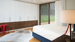 A bedroom with a bed, a ceiling fan, a nightstand, a lamp, a red stool, and a large window with a view of a lawn. - Mid-Century Home Surrounded by Meadows (Pine Plains)