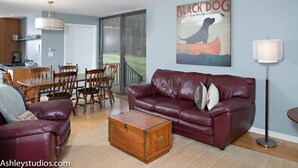 A living room with a leather sofa, a wooden coffee table, a dining table with chairs, and a kitchen in the background. - Mid-Century Home Surrounded by Meadows (Pine Plains)