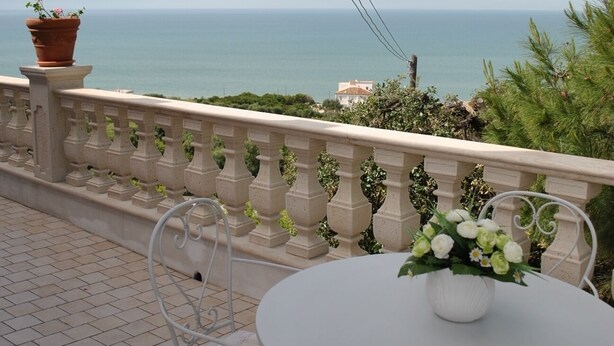 Een terras met een ronde tafel en stoelen, met uitzicht op de kust.