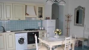Een compacte keuken met een wasmachine, een eettafel met stoelen en een kroonluchter.