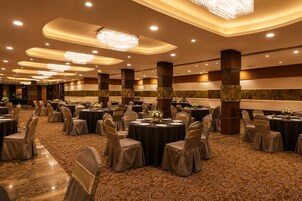 Un salón de banquetes con mesas redondas, sillas y candelabros.