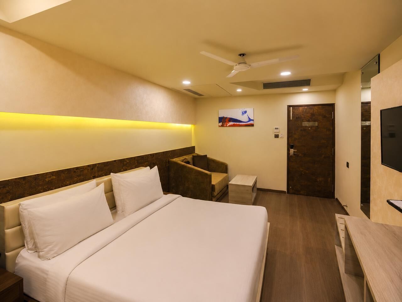 A hotel room with a bed, a desk, a chair, a television, and a door.