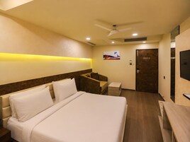 A hotel room with a bed, a desk, a chair, a television, and a door.