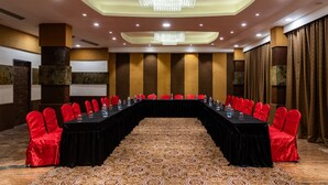 Une salle de conférence avec une longue table, des chaises rouges et un tapis à motifs.