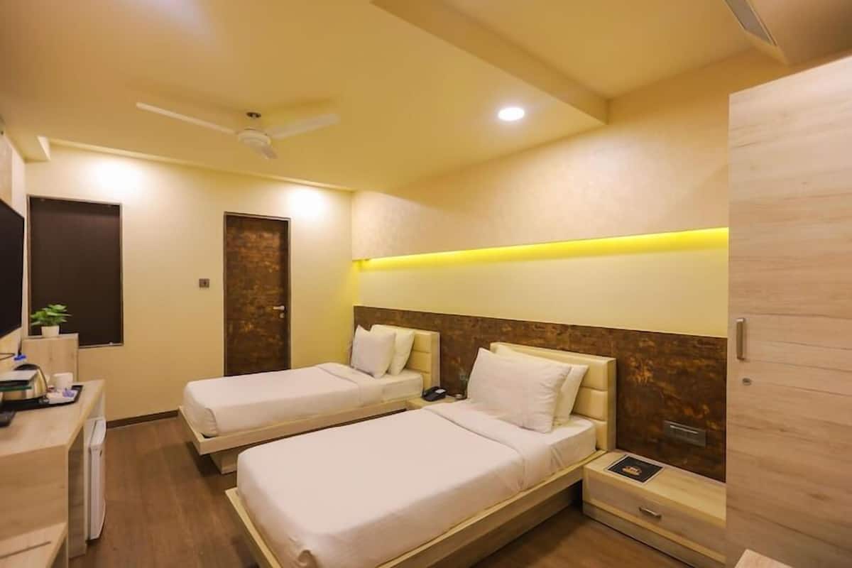 A hotel room with two single beds, a desk with a computer, a small table, and a TV.