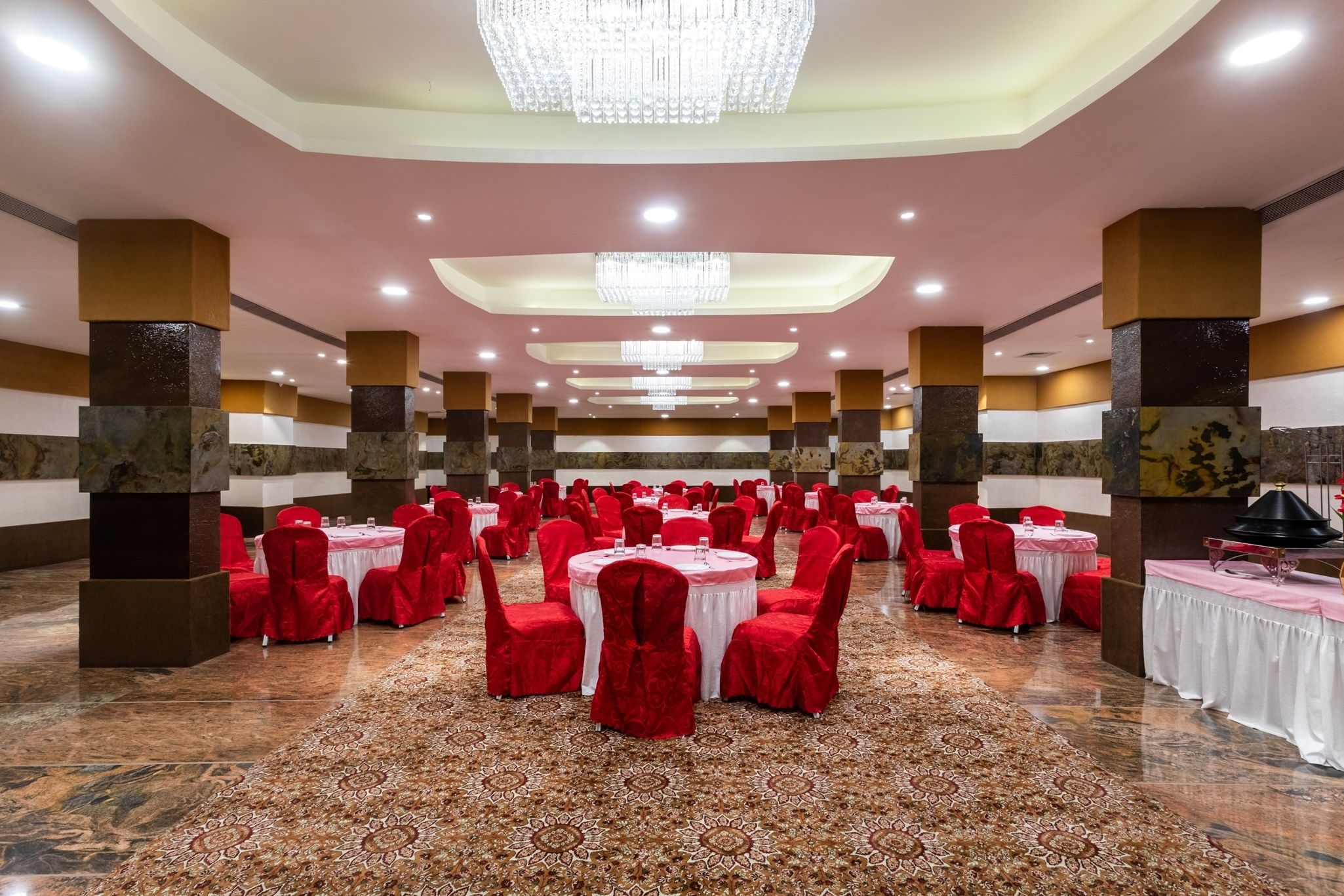 Un salón de banquetes con mesas redondas, sillas rojas y candelabros.