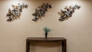 Un espace d’accueil avec une console en bois foncé, une petite plante en pot et trois œuvres d’art murales représentant des papillons.